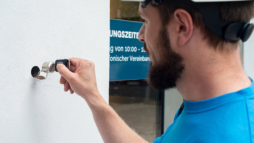 Haushahn Techniker mit Helm am Schlüsseldepot an der Außenwand eines Gebäudes