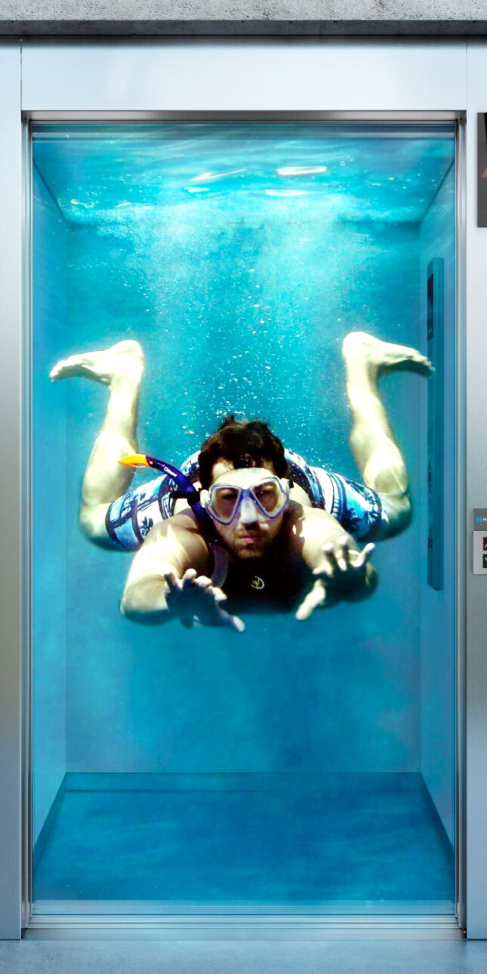 Eine Person mit Schwimmbrille und Shorts schwimmt in einem gläsernen Aufzug unter Wasser und streckt sich nach vorne, als würde sie schwimmen, während die Aufzugstüren geöffnet sind und der Raum mit Wasser gefüllt ist.