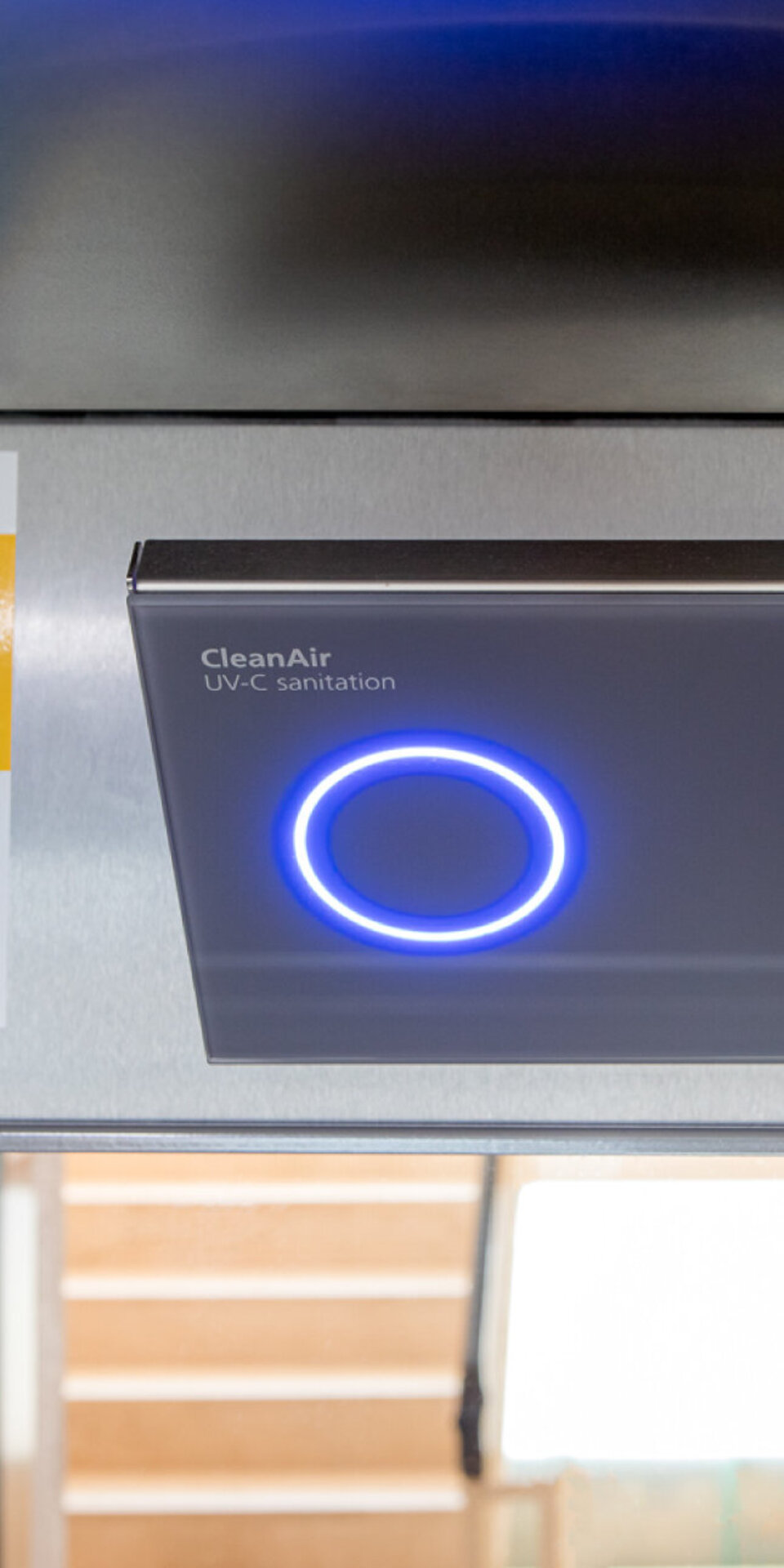 Eine Nahaufnahme eines modernen UV-C-Luftreinigungsgeräts mit einem blau leuchtenden Ring und einem Schild daneben, auf dem "Hygienische Kabinenluft mit UV CleanAir" steht.