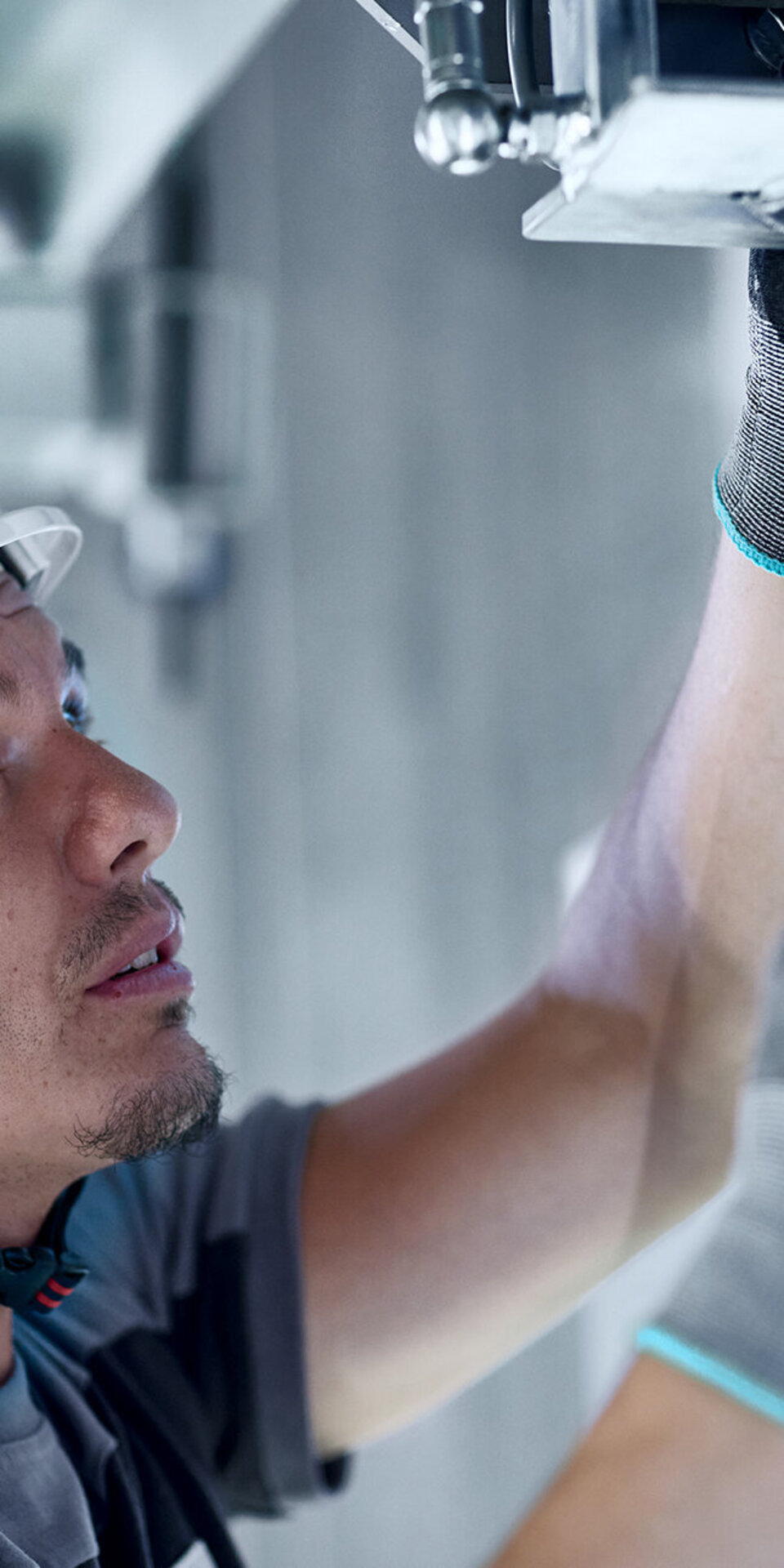 Ein Bauarbeiter mit weißem Schutzhelm und Sicherheitshandschuhen richtet die Metallgeräte über dem Kopf aus und schaut aufmerksam nach oben, während er in einem Gebäude arbeitet.